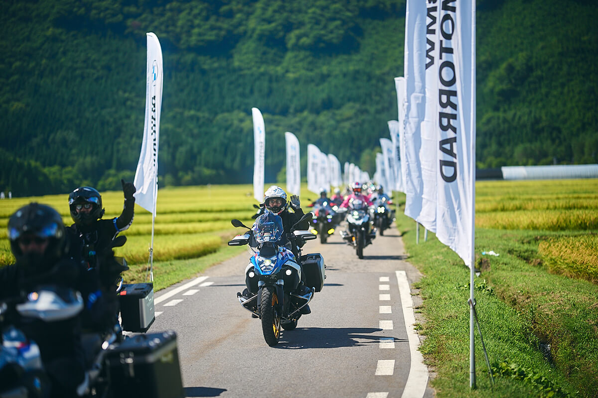 会場に向かうルートの脇に上り旗が立ちライダーが手を振る画像